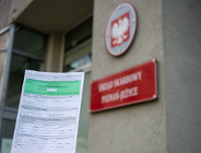 Na zdjęciu formularz PIT trzymany w dłoni, w tle urząd skarbowy