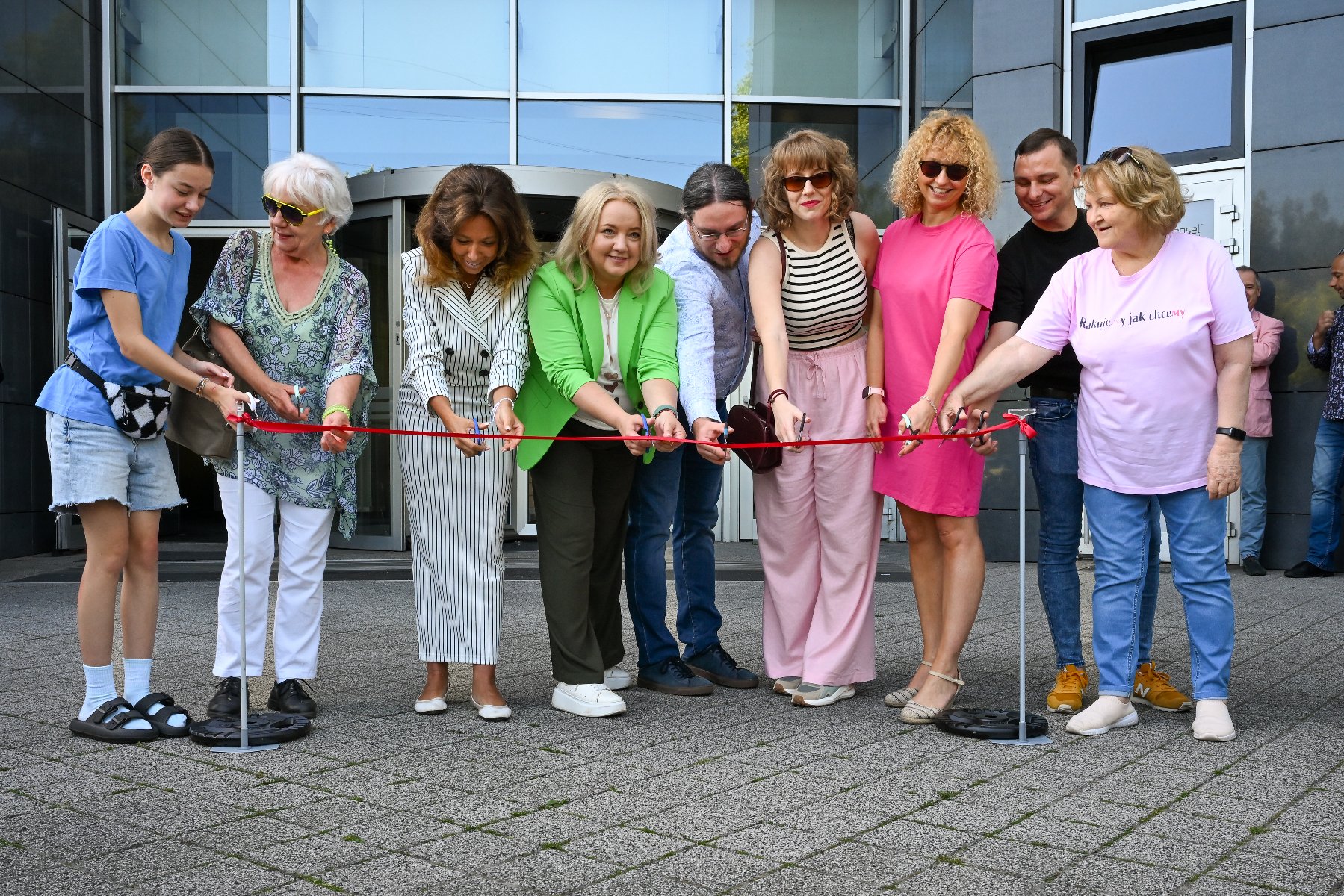 Na zdjęciu grupa ludzi przecinających wstęgę, za nimi szklana fasada biurowca