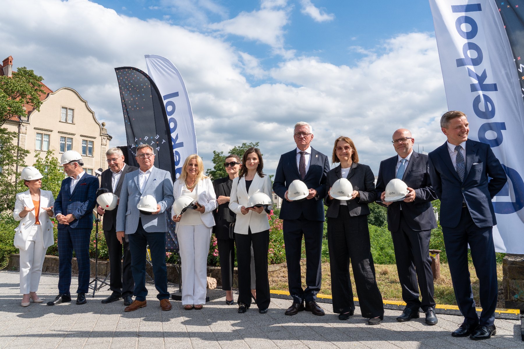 Na zdjęciu grupa mężczyzn i kobiet pozująca do obiektywu z kaskami budowlanymi w dłoniach