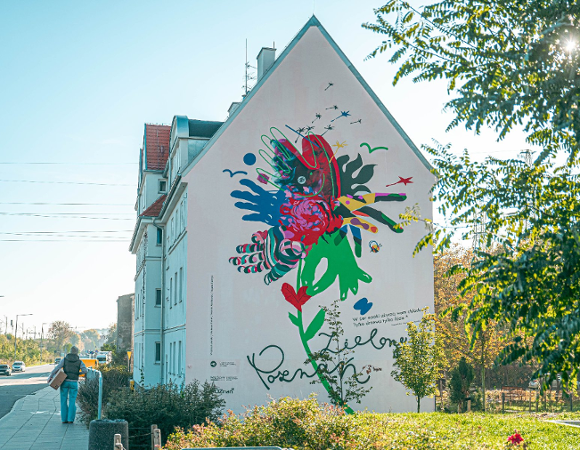 Na zdjęciu kamienica, na jej bocznej ścianie kolorowy mural - splecione dłonie