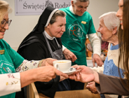 Na zdjęciu ludzie podający sobie herbatę lub kawę, wśród nich siostra zakonna