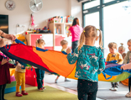 Na zdjęciu małe dzieci bawiące się kolorową chustą