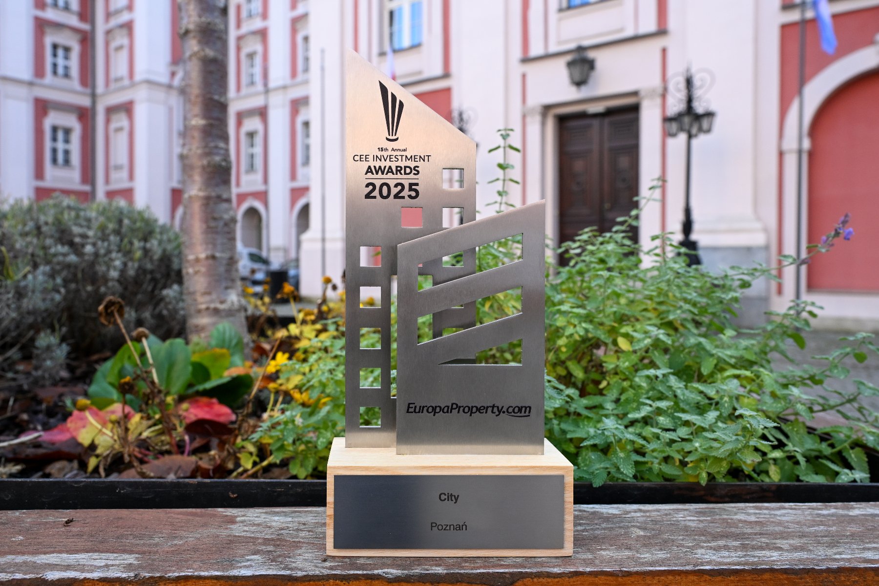 Na zdjęciu metalowa statuetka na tle zieleni i budynku urzędu miasta