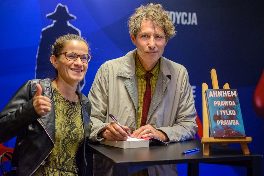 na zdjęciu mężczyna i kobieta poczas spotkania, uśmiechają się, przed nimi leży książka, wpisują dedykacje i autografy