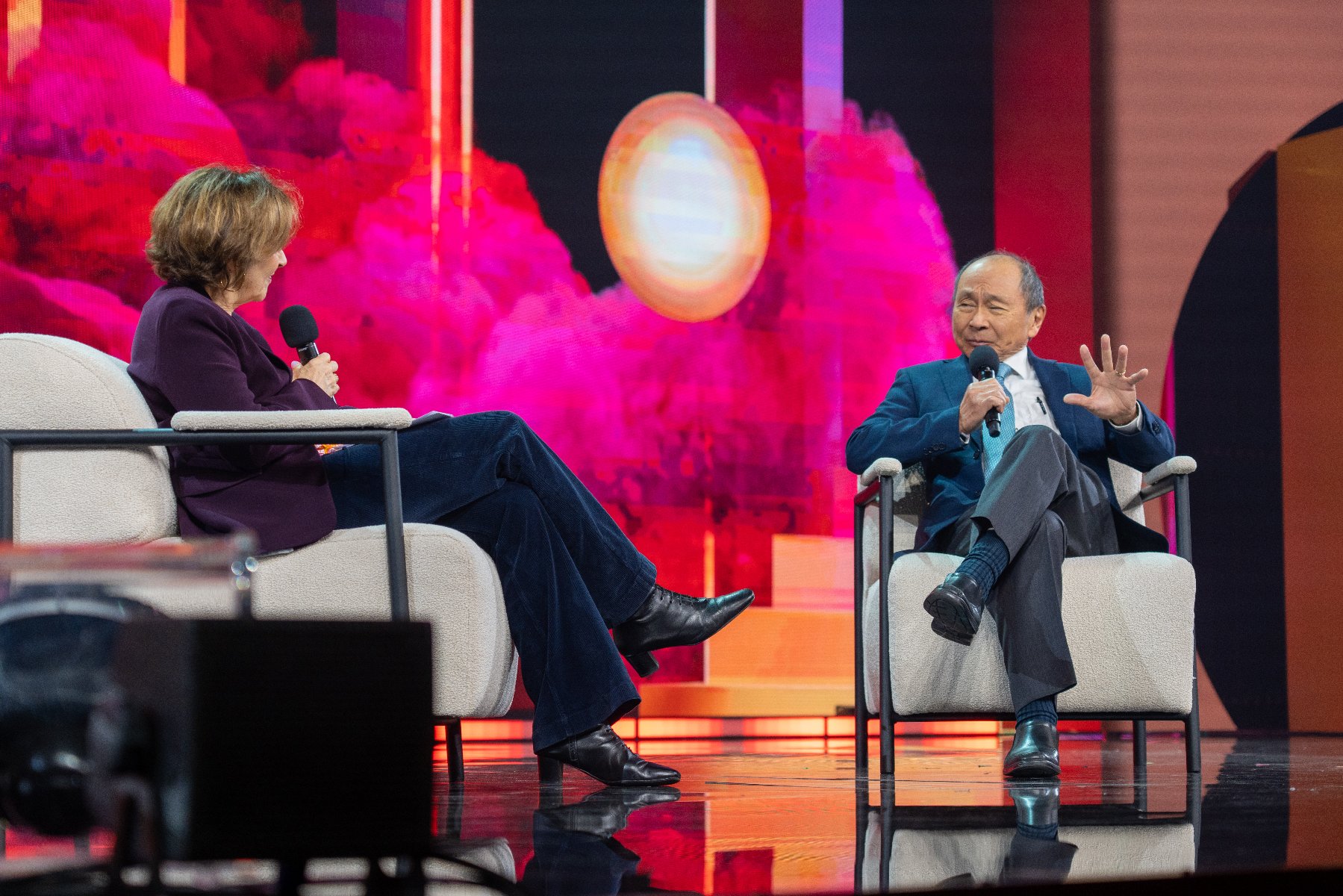 Na zdjęciu mężczyzna i kobieta na scenie, siedzą na krzesłach, rozmawiają