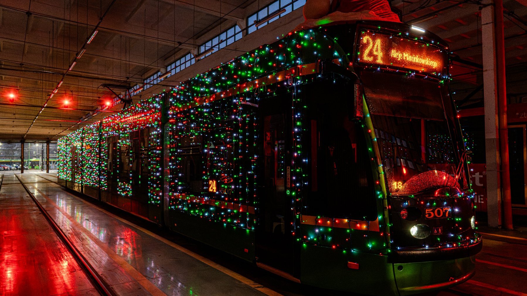 Na zdjeciu rozświetlony tramwaj w czerwonej czapce Mikołaja.