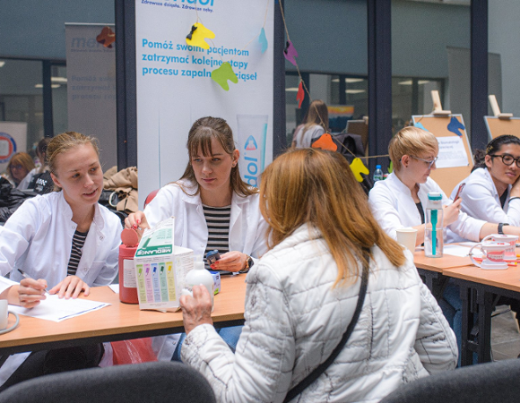 Na zdjęciu stoisko, przy nim trzy kobiety, dwie z nich noszą lekarskie fartuchy