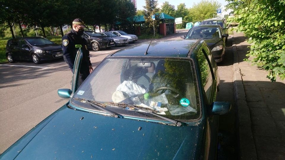 Na zdjęciu strażnik miejski stoi przy samochodzie, w którym przebywa osoba bezdomna. Zdjęcie zrobiono w pandemii covid 19, zdjęcie archiwalne