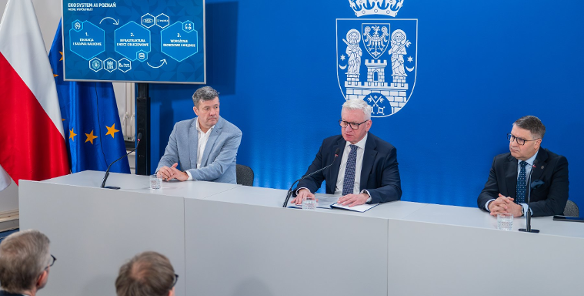 Na zdjęciu trzej mężczyźni w garniturach, siedzący za stołem podczas konferencji prasowej