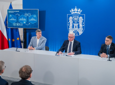 Na zdjęciu trzej mężczyźni w garniturach, siedzący za stołem podczas konferencji prasowej