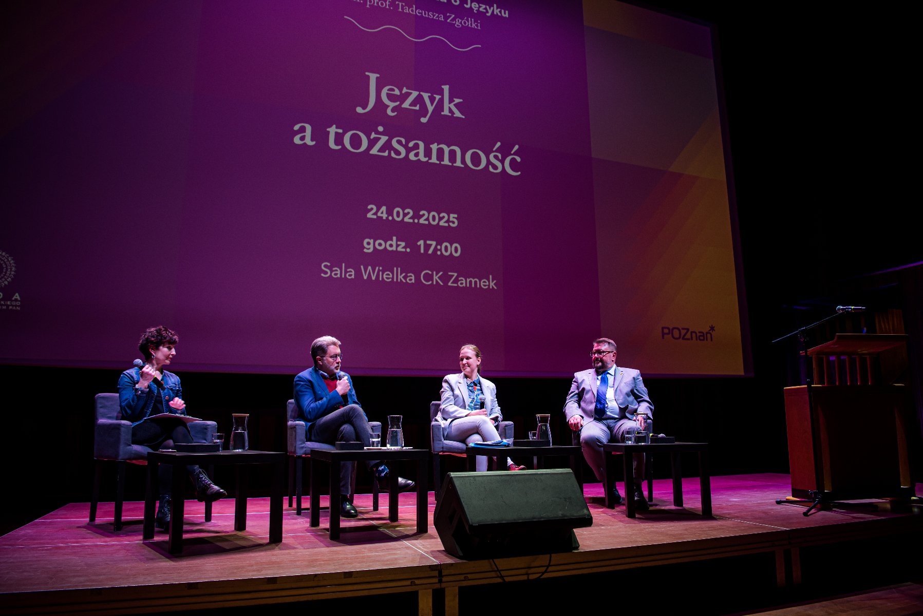 Na zdjeciu trzy osoby siedzące na krzesłach na scenie