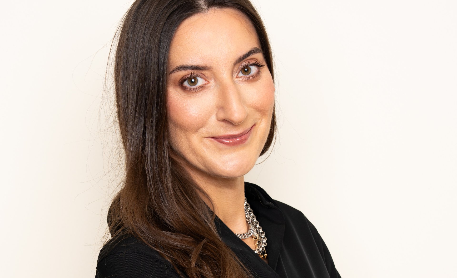 Na zdjeciu uśmiechnięta kobieta o ciemnych włosach patrząca w obiektyw, zdjęcie portretowe