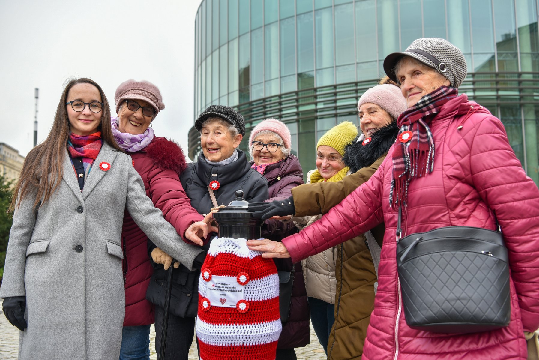 Na zdjeciu uśmiechnięte kobiety, trzymające hydrant w szydełkowym ubranku
