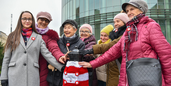 Na zdjeciu uśmiechnięte kobiety, trzymające hydrant w szydełkowym ubranku