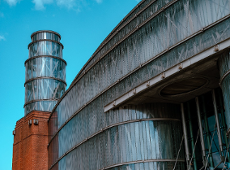 Na zdjęciu widać fragment fasady centrum hanli i sztuki Starty Browar. Fasada jest wykonana z szkła i stali. Widać również fragment ceglanej ściany. W tle widać błękitne niebo.