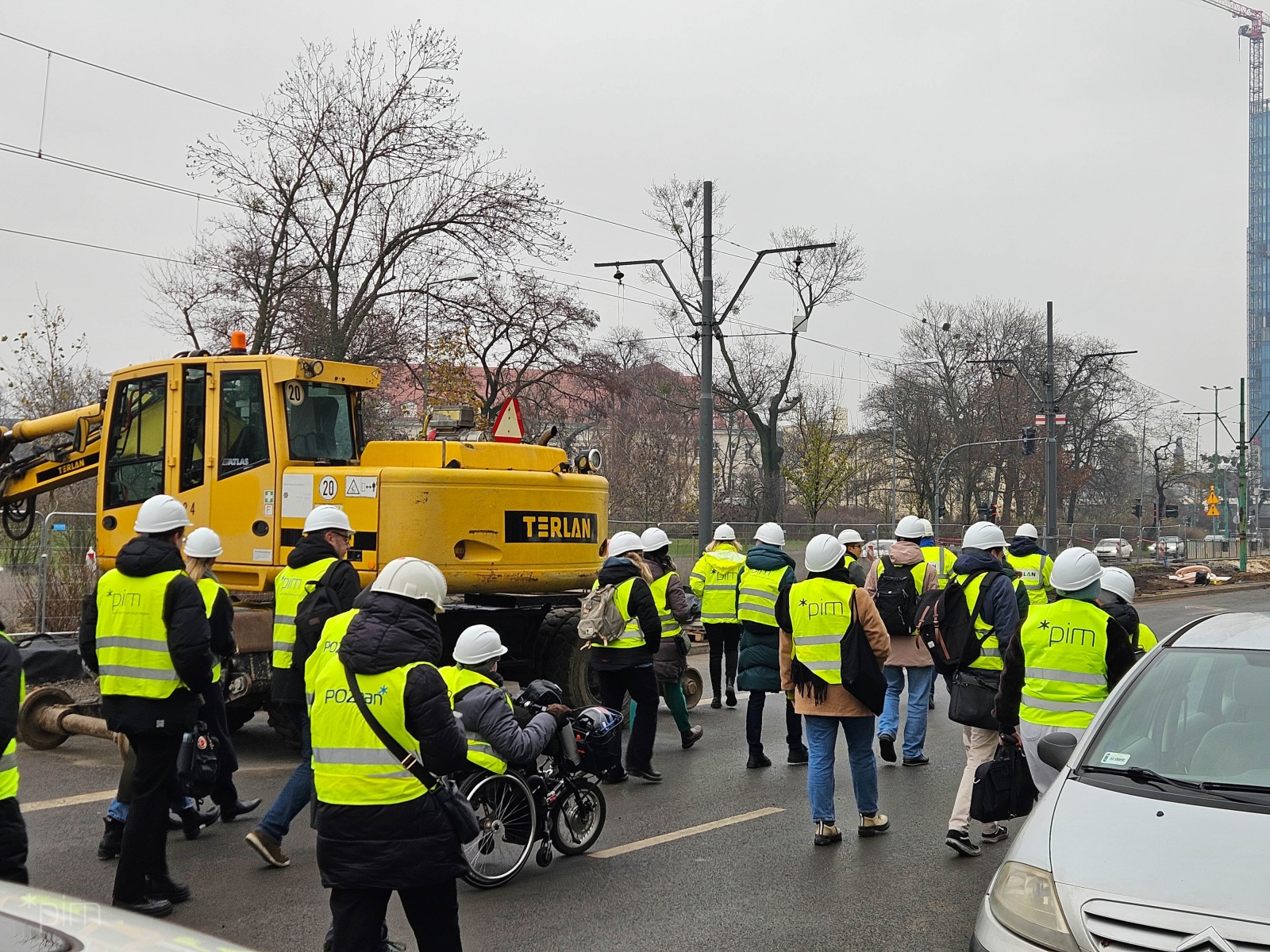 Na zdjęciu widać kilkunastu uczestników wizytacji ubranych w odblaskowe kamizelki i kaski. W tle widać koparkę oraz linię tramwajową.