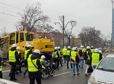 Na zdjęciu widać kilkunastu uczestników wizytacji ubranych w odblaskowe kamizelki i kaski. W tle widać koparkę oraz linię tramwajową.