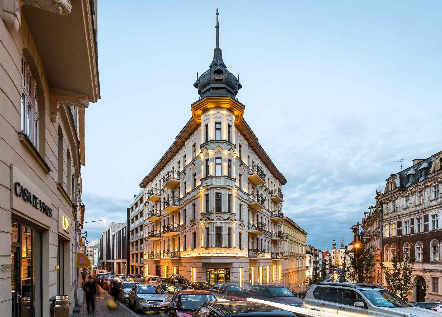 Na zdjęciu widać podświetloną kamienice. Pod budynkiem ruch samochodowy.