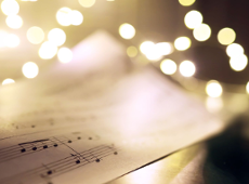 Na zdjęciu widać zapis nutowy oraz lampki świąteczne w ciepłym kolorze