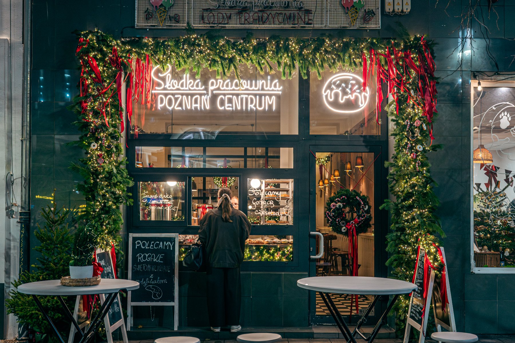 Na zdjęciu witryna ozdobiona girlandą, widać kobietę kupującą coś przez okienko