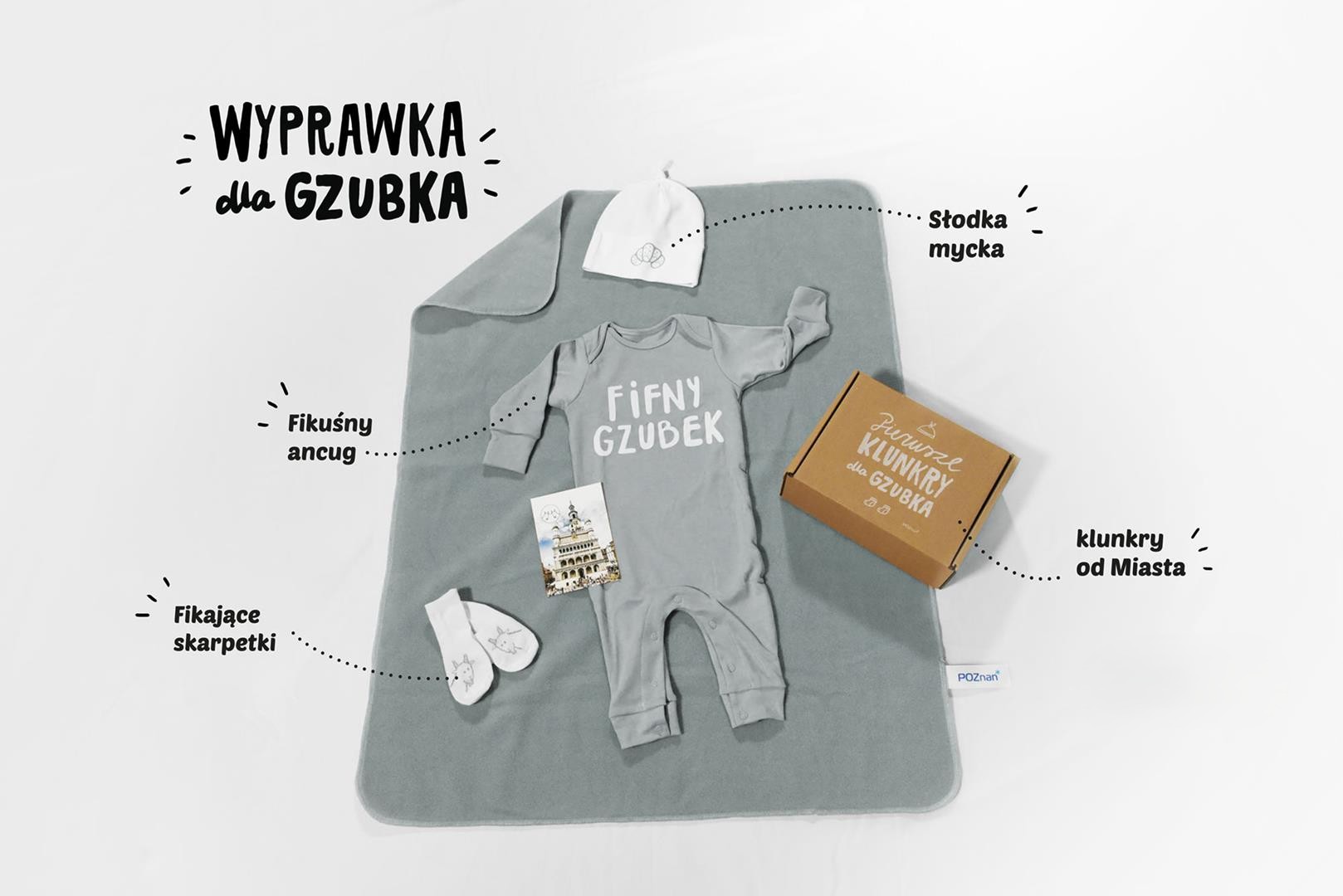 Na zdjęciu wyprawka: na stoliku rozłożone śpioszki i inne elementy wyprawki, w tle widać rośliny