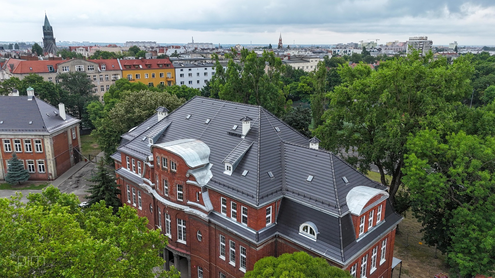 Na zdjęciu zabytkowy budynek z nowym dachem, widziany z lotu ptaka, w tle drzewa