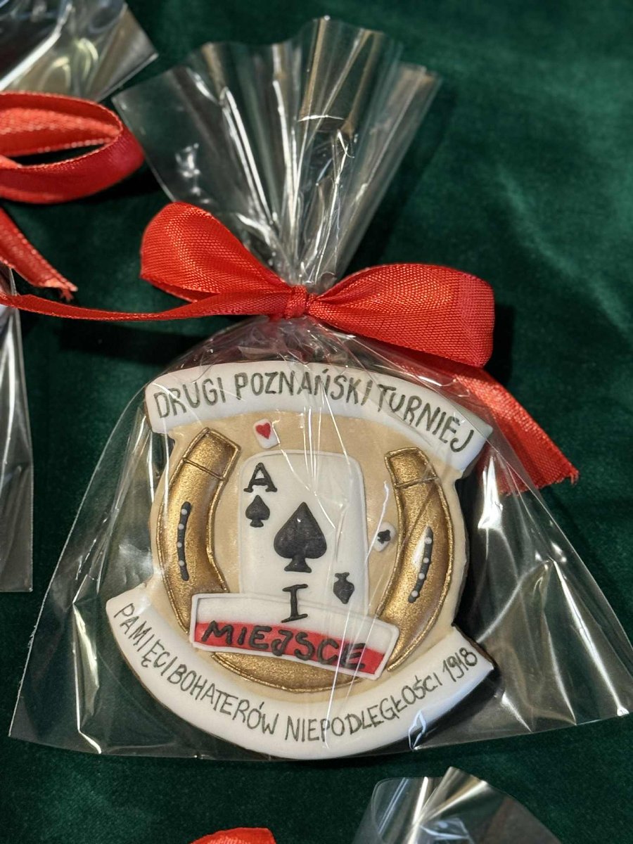 Nagrody w II Turnieju Pamięci Bohaterów Niepodległości 1918, fot. City Park Bridge Club - zdjęcie piernika z motywem podkowy i asa na beżowym tle. Wszystko na tle zielonego materiału
