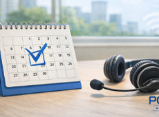 obrazek przedtawia kalendarz oraz słuchawki nagłowne z mikrofonem stojące na biurku, w tle widać okno z zielenią