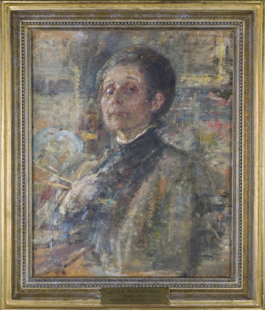 Odwrócona tyłem młoda kobieta siedzi na krześle, ma brązowe upięte włosy, a jej twarz wyraża smutek lub tęsknotę, w rękach trzyma bukiet białych tulipanów.