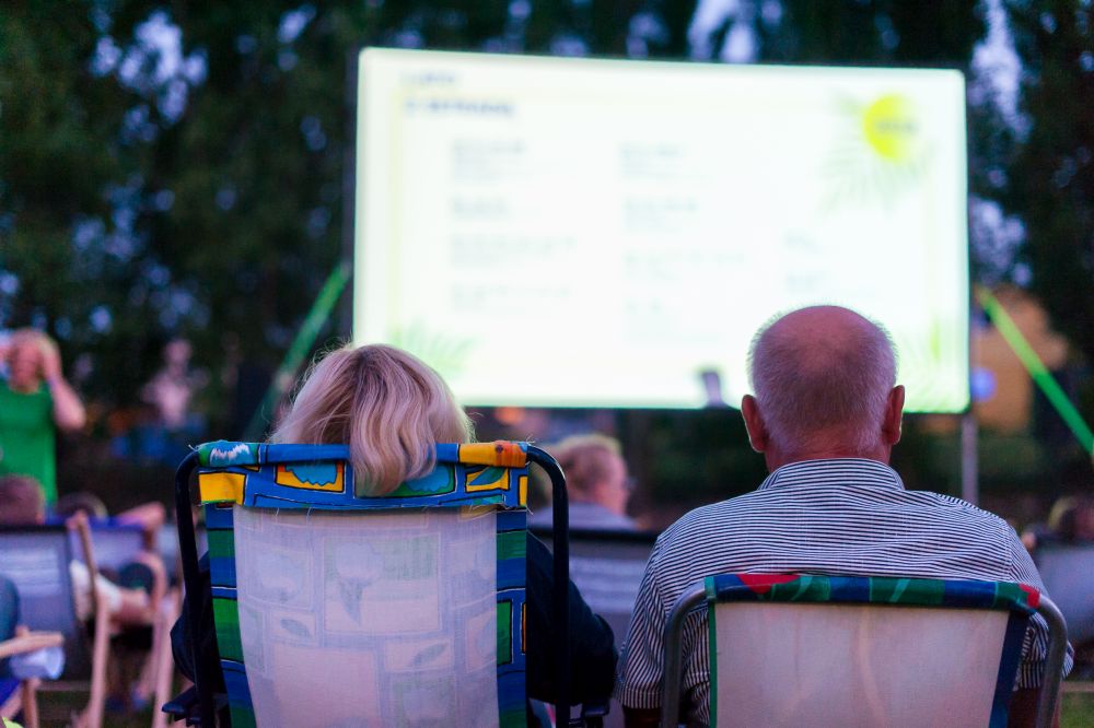 Para starszych ludzi ogląda film w plenerze siedząc na leżakach.