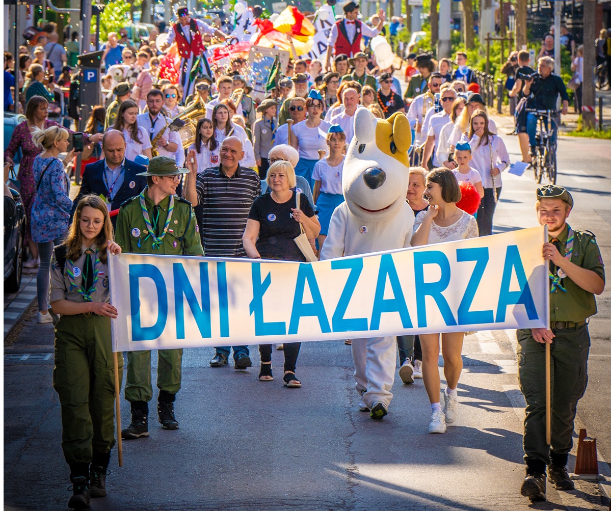 Parada mieszkańców Łazarza. Na czele przemarszu para harcerzy niesie transparent z napisem Dni Łazarza. Z nimi idą uczestnicy parady.