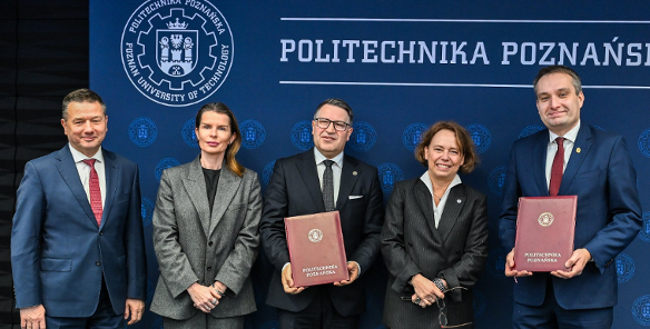 Pięć osób w biznesowych strojach (trzech mężczyzn i dwie kobiety) stoi na tle ciemnoniebieskiej ściany z logotypem i napisem "POLITECHNIKA POZNAŃSKA". Mężczyzna w środku i mężczyzna po prawej trzymają w dłoniach dokumenty oprawione w bordową skórę.