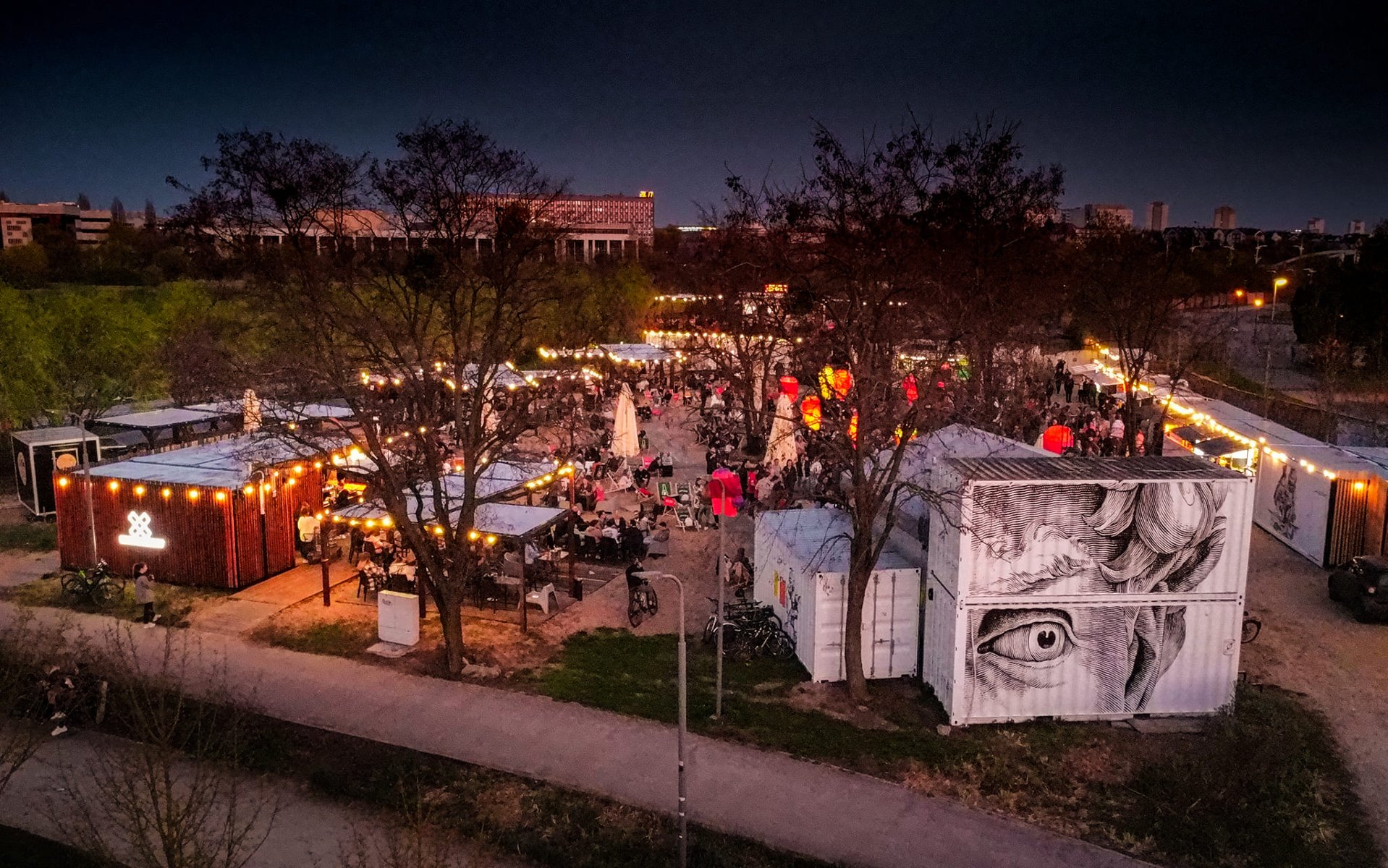 Plaża miejska nocą. Kontenery, dyużo świateł, leżaki, lampiony. Widok z góry.