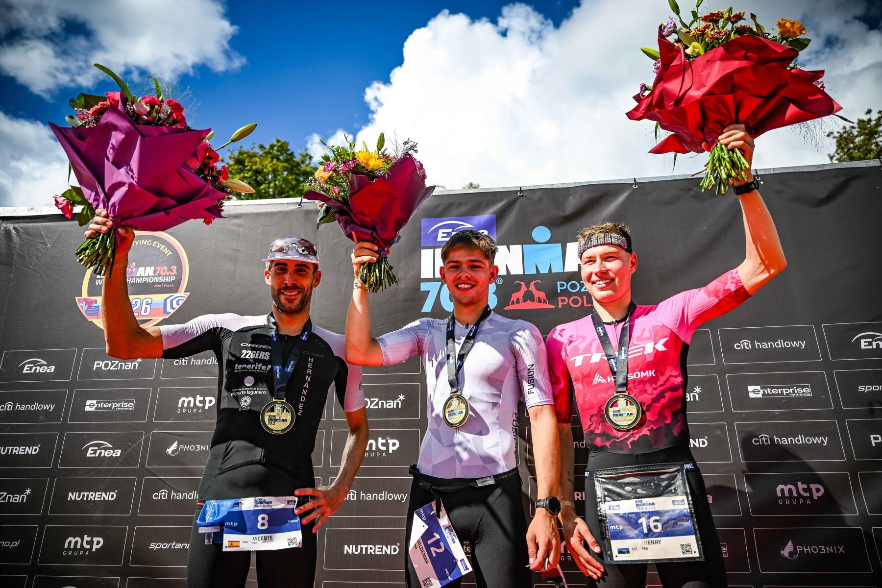 Podium Enea IRONMAN 70.3 Poznań wśród mężczyzn, fot. IRONMAN Poland - 3 mężczyzn stoi na podium z kwiatami i medalami na szyi