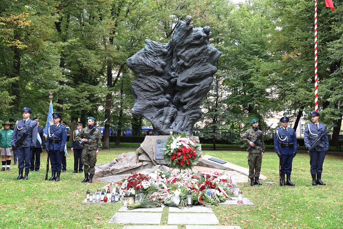 przed pomnikiem straż pełnią żołnierze w mundurach różnych rodzajów sił zbrojnych wokół trawa i drzewa