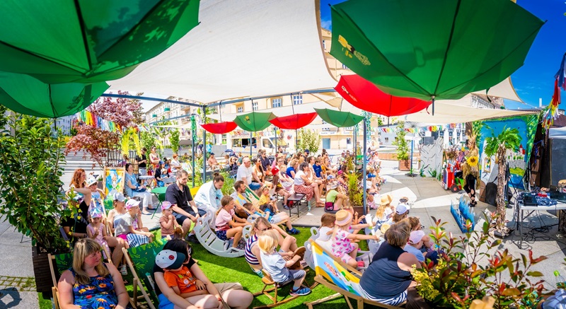 Publciczność siedząca na leżackach. Przed nimi wstęp dla dzieci. Strefa przystrojonwa jest powieszonymi nad ich głowami kolorowymi prasalami.