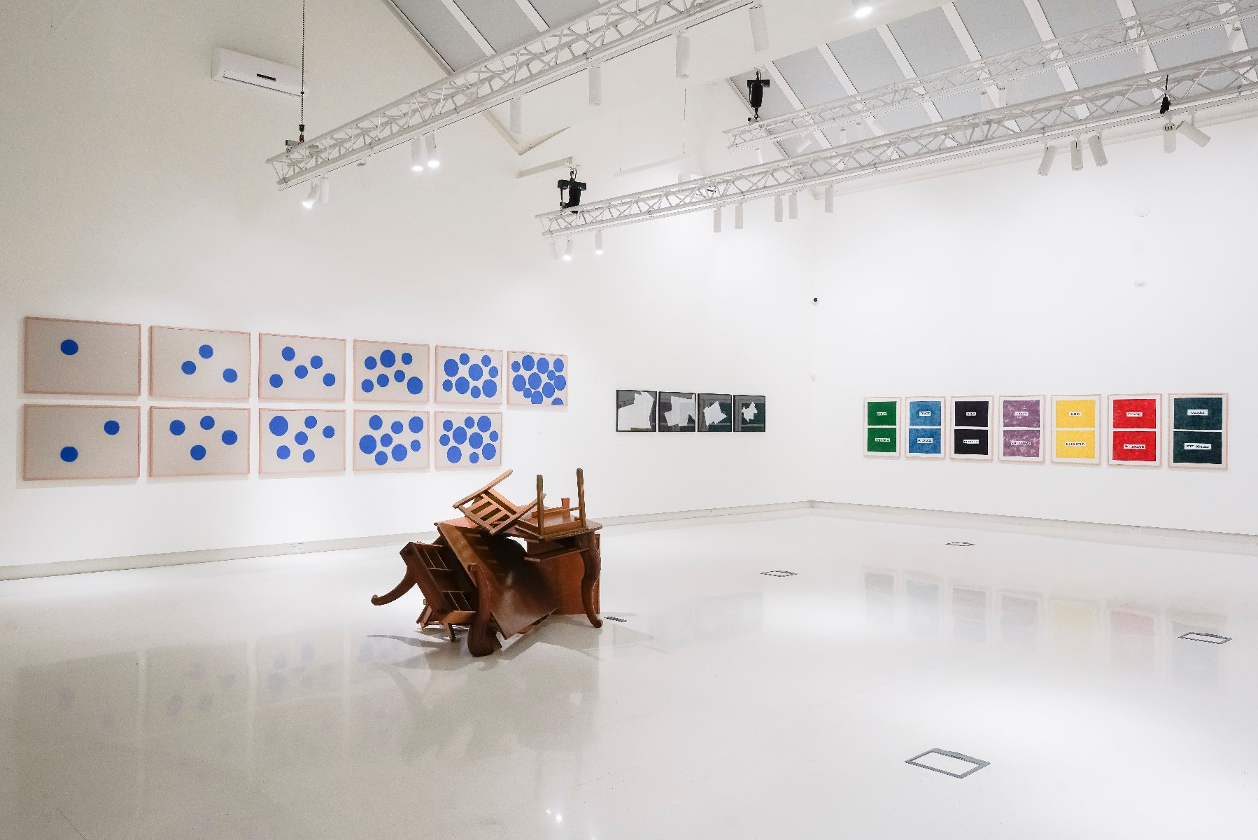 Rzeźba ułożona z krzeseł i obrazy na ścianach galerii