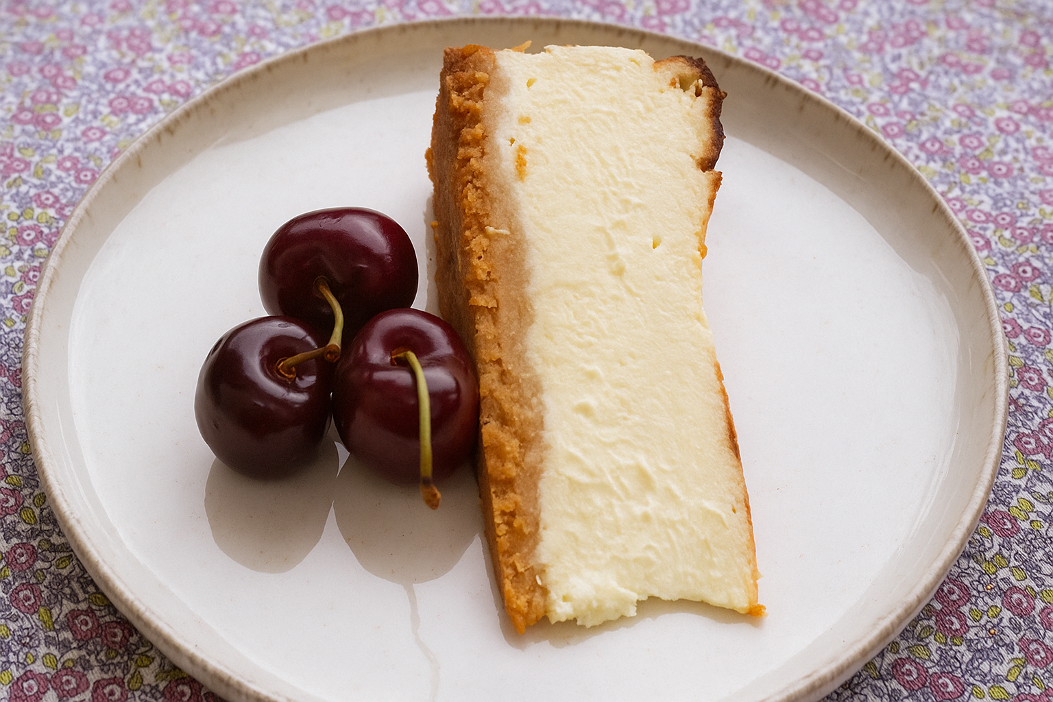 Sernik baskijski z kremowym wnętrzem, obok trzy czereśnie.