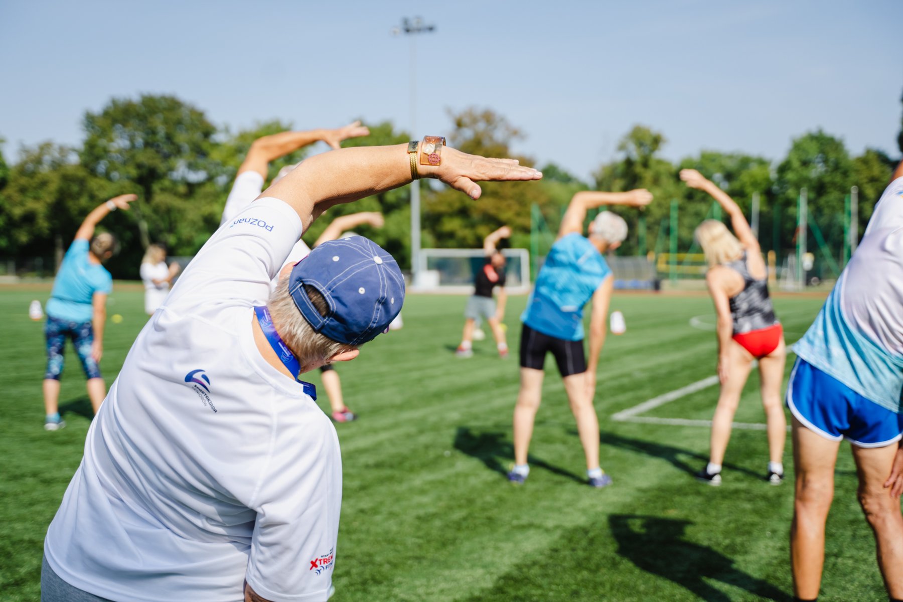 Spartakiada Seniorów, fot. Agnieszka Wojt-Kaczmarek - kilkoro seniorów ćwiczy gimnastykę na murawie w strojach sportowych w słonecznej pogodzie