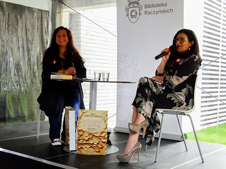 Dwie kobiety siedzące na krzesłach w Bibliotece Raczyńskich. Jedna z nich trzyma w ręce mikrofon.