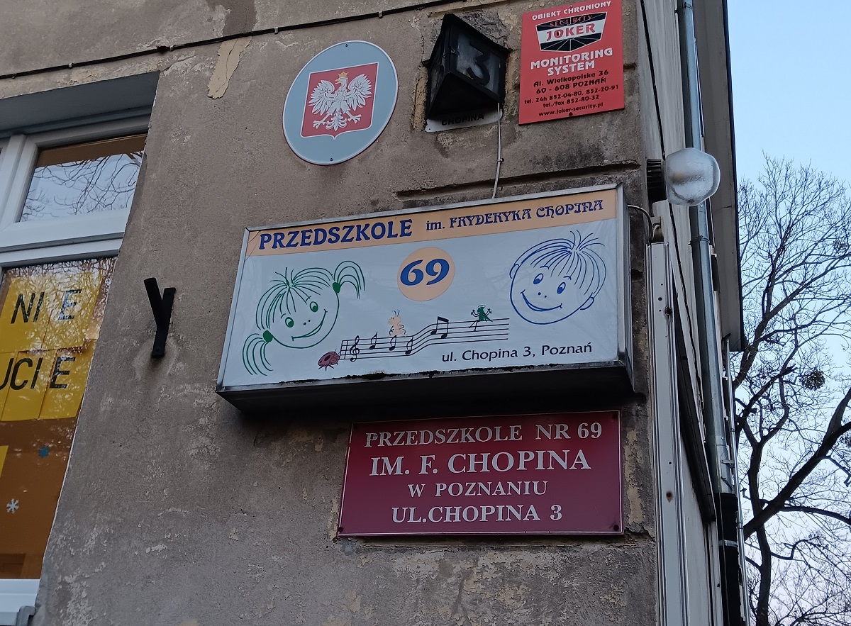 Szyld przedszkola nr 69 na fasadzie budynku, widać też tablice z godłem Polski