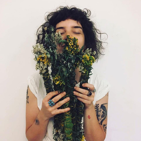 Młoda kobieta trzyma w ręku bukiet roślin i wdycha ich zapach.