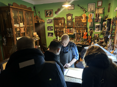 Uczestnicy wizyty studyjnej z Serbii przy stole, wspólnie oglądająca instrument muzyczny w pracowni lutniczej.