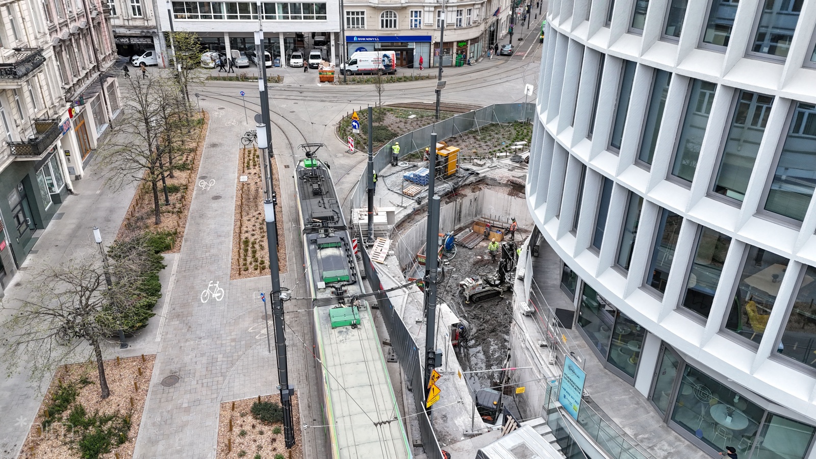 Ujęcie z góry na prace na placu budowy przy Okrąglaku. Po prawej stronie widać budynek okrąlaka, u dopłu pracowników na placu budowy, po środku torowisko tramwajowe, po lewej kamienice.