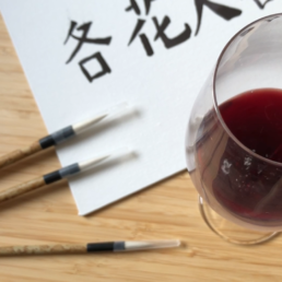 Kartka papieru a na niej chińska kaligrafia, obok kieliszek z czerwonym napojem.