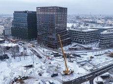 Widok z lotu ptaka na remonowane ulice. W centralnej części ujęcia widać dzwig i maszyny remontowe. W tle wysokie budynki i kamienice - panorama miasta. Wszystko w zimowej scenerii, przysypane śniegiem.