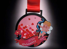 Wizualizacja medalu XI Biegu Walentynkowego - na ciemnym tle jest medal z wizerunkiem amorka, a także małymi czerwonymi sercami na różowym tle