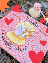 Okładka książki o słoniu Pomelo. W centralnej części słoń i jego przyjaciel, dookoła czerwone serduszka. Napis: Pomelo i niezwykły skarb.