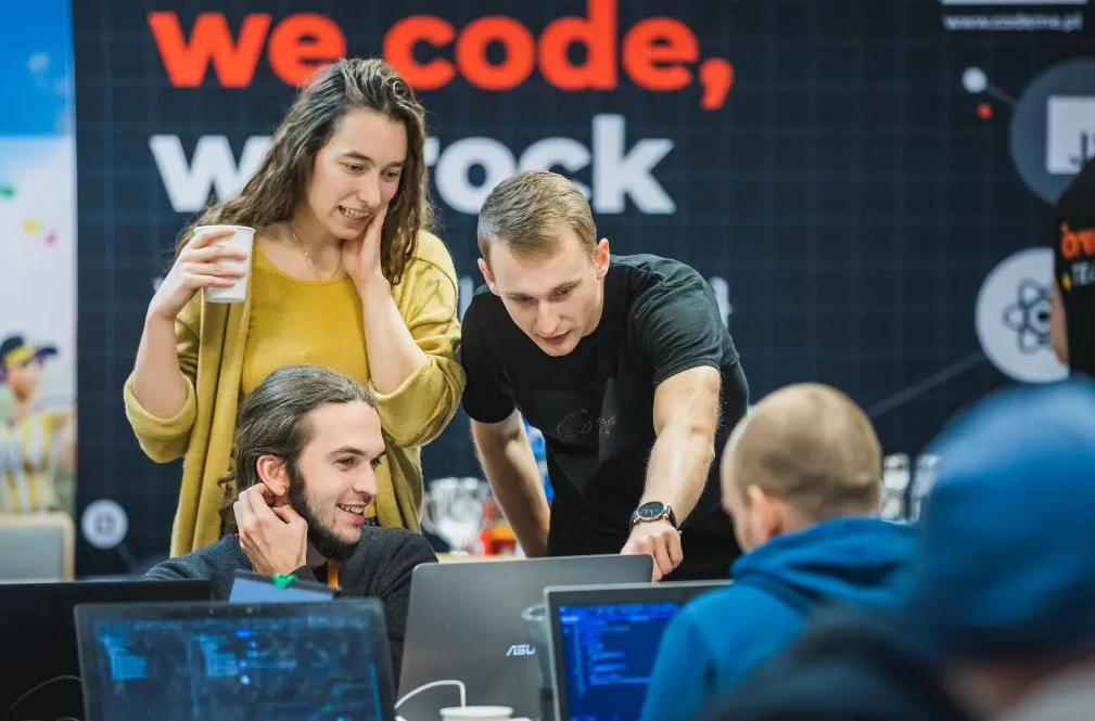 Dwóch mężczyzn i kobieta stoją przy stanowisku komputerowym. Rozmawiają na temat tego, co widzą na ekranie.