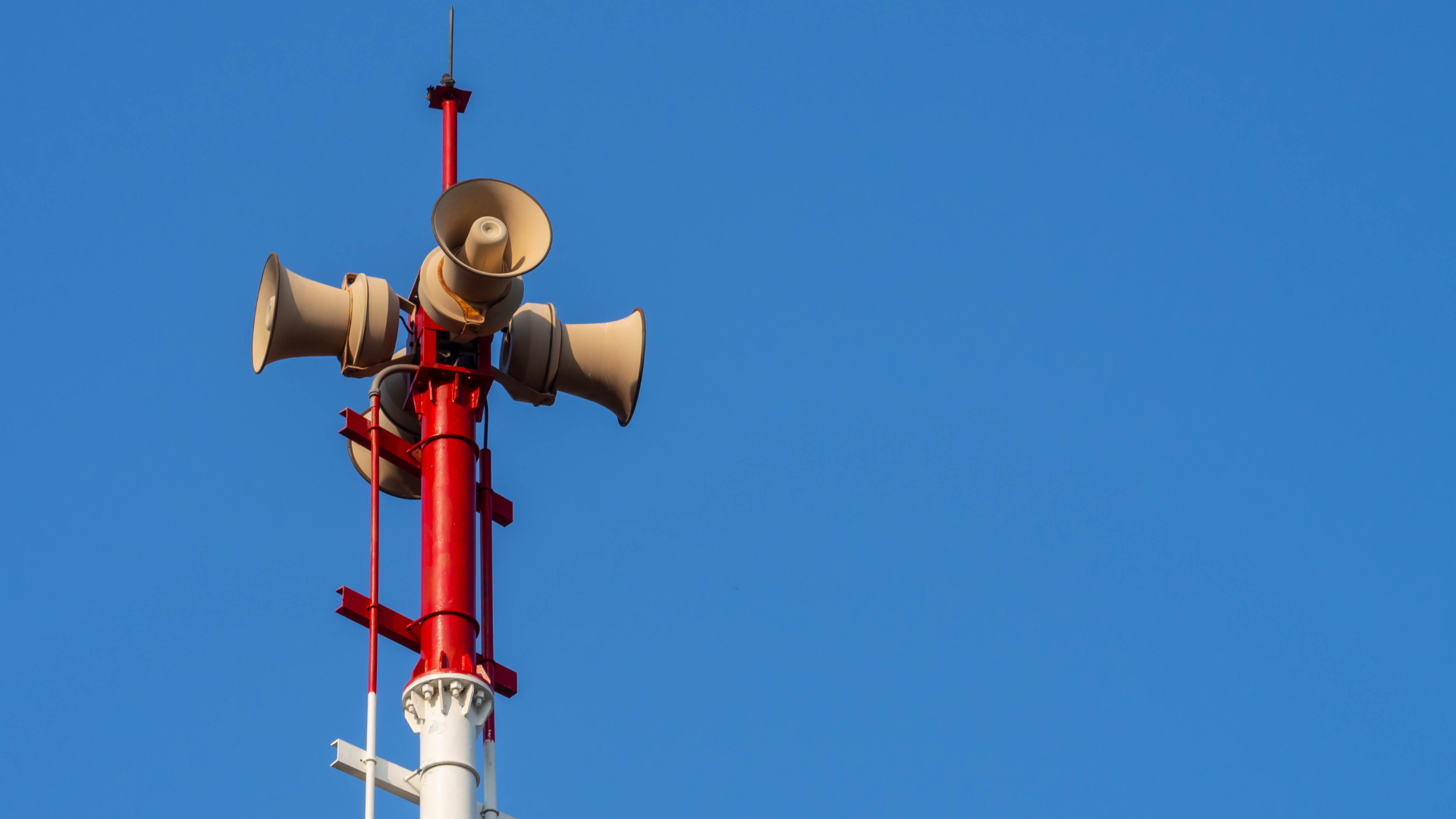 Zdjęcia czerwono-białego słupa syreny alarmowej na tle niebieskiego nieba